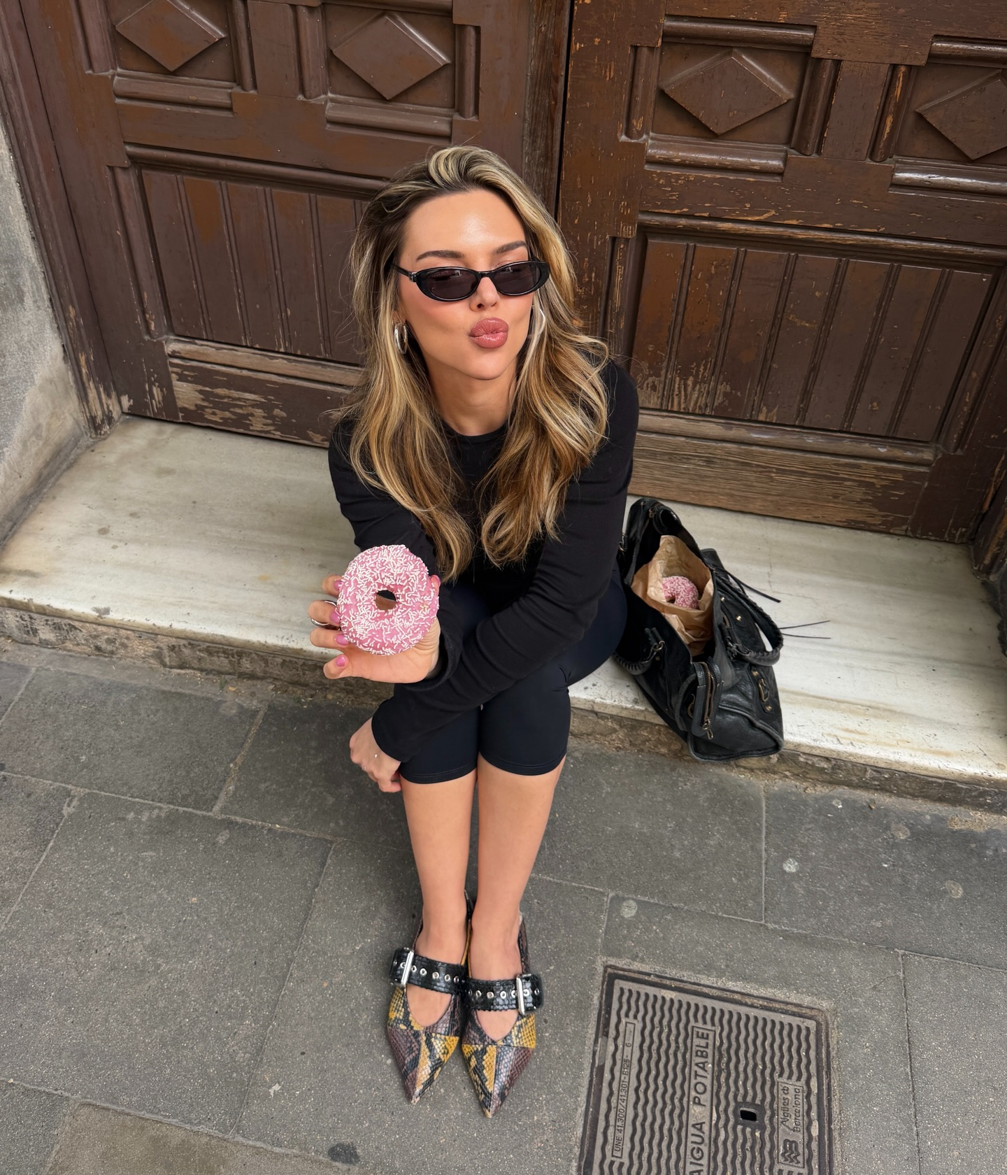 Simla with sunglasses and a pink doughnut against an old wooden doorway