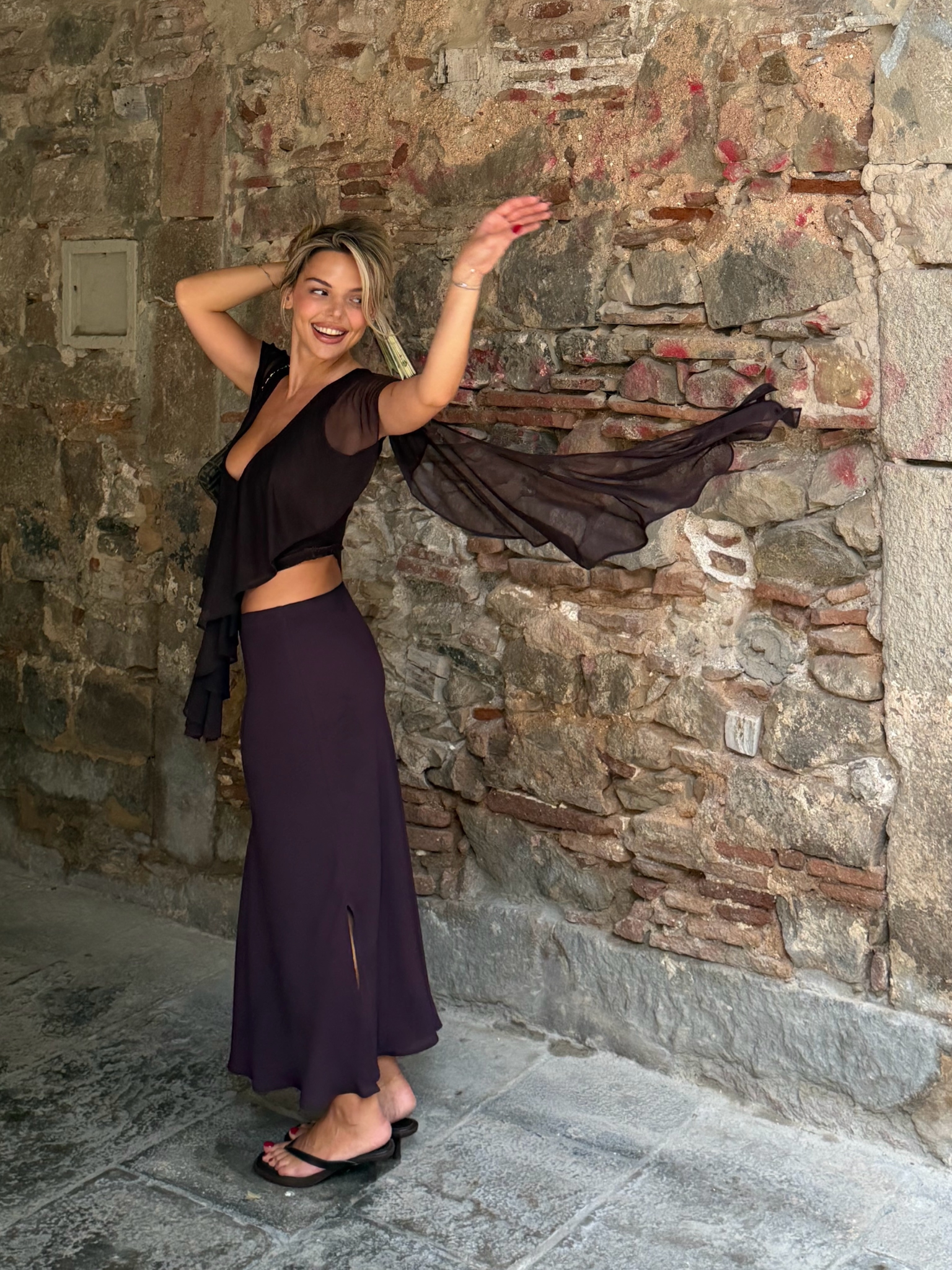 Simla in a flowing black outfit against a textured stone wall